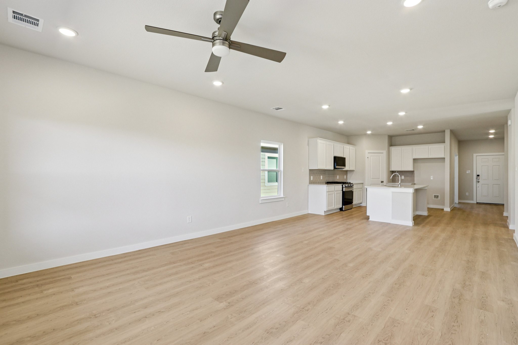 A large empty room with a ceiling fan and a wood floor.
