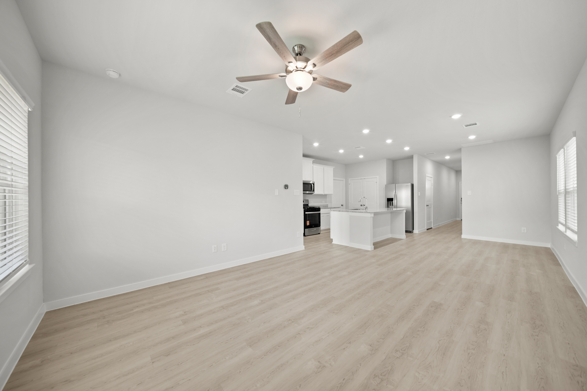 A large empty room with a ceiling fan and a wood floor.